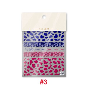 Op de afbeelding: Een pakketje met nagelstickers met een koe-print ontwerp. De stickers zijn blauw en roze en hebben de tekst "Cute Cow" erop. Het pakketje is gelabeld met het nummer "#3".