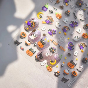 Peut inclure: Une feuille d'autocollants pour ongles sur le th&egrave;me d'Halloween avec une vari&eacute;t&eacute; de motifs, notamment des chats noirs, des citrouilles, des fant&ocirc;mes et des &eacute;toiles. Les autocollants sont sur un fond transparent et ont une finition brillante.