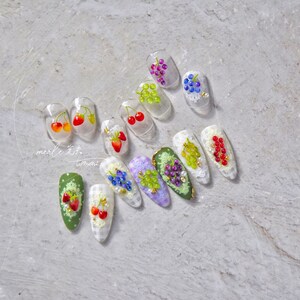 Pu&ograve; includere: Un set di 12 unghie finte con diversi design di frutta. Le unghie sono trasparenti e hanno un design di pizzo bianco. I frutti includono ciliegie, fragole e uva.