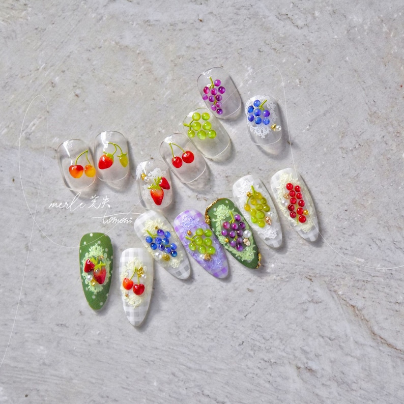 Pu&ograve; includere: Un set di 12 unghie finte con diversi design di frutta. Le unghie sono trasparenti e hanno un design di pizzo bianco. I frutti includono ciliegie, fragole e uva.
