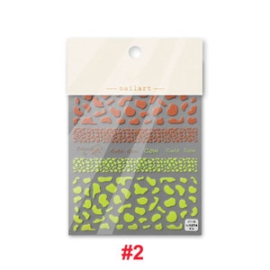 Op de afbeelding: Een pakketje met nagelstickers met een koe-print in oranje en groen. Het pakketje heeft de tekst "nailart" en "cute cow" erop. De sticker sheet is gelabeld met het nummer "#2".