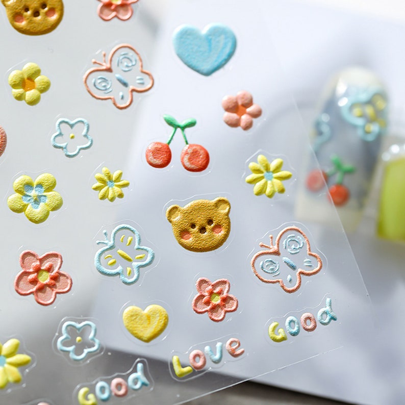 May include: A sheet of colorful, 3D puffy stickers with various designs, including butterflies, hearts, flowers, cherries, and a bear. The stickers have the words "Good" and "Love" written on them.