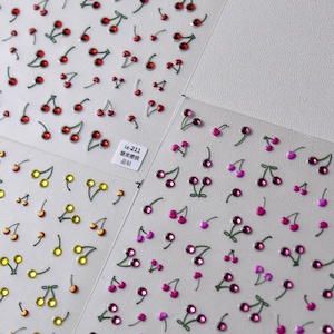 May include: Two sheets of nail art stickers with cherry designs. One sheet features red cherries and the other sheet features pink cherries. The text on the sheet reads "ta-211 糖果櫻桃 晶钻".