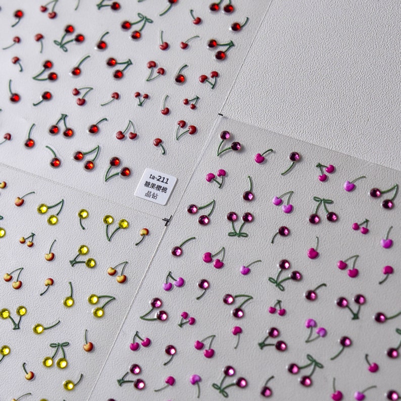 May include: Two sheets of nail art stickers with cherry designs. One sheet features red cherries and the other sheet features pink cherries. The text on the sheet reads "ta-211 糖果櫻桃 晶钻".