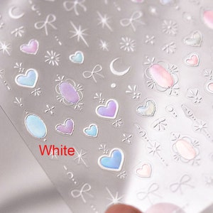 May include: A sheet of clear stickers with a variety of designs, including hearts, stars, bows, and moons. The stickers are iridescent and have a white background.