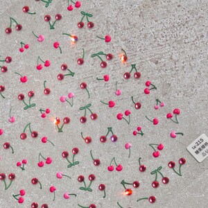 May include: A sheet of clear adhesive paper with a repeating pattern of pink and red cherries with green stems. The sheet has a label in the bottom right corner that reads "ta-215  贴纸装饰  贴纸"