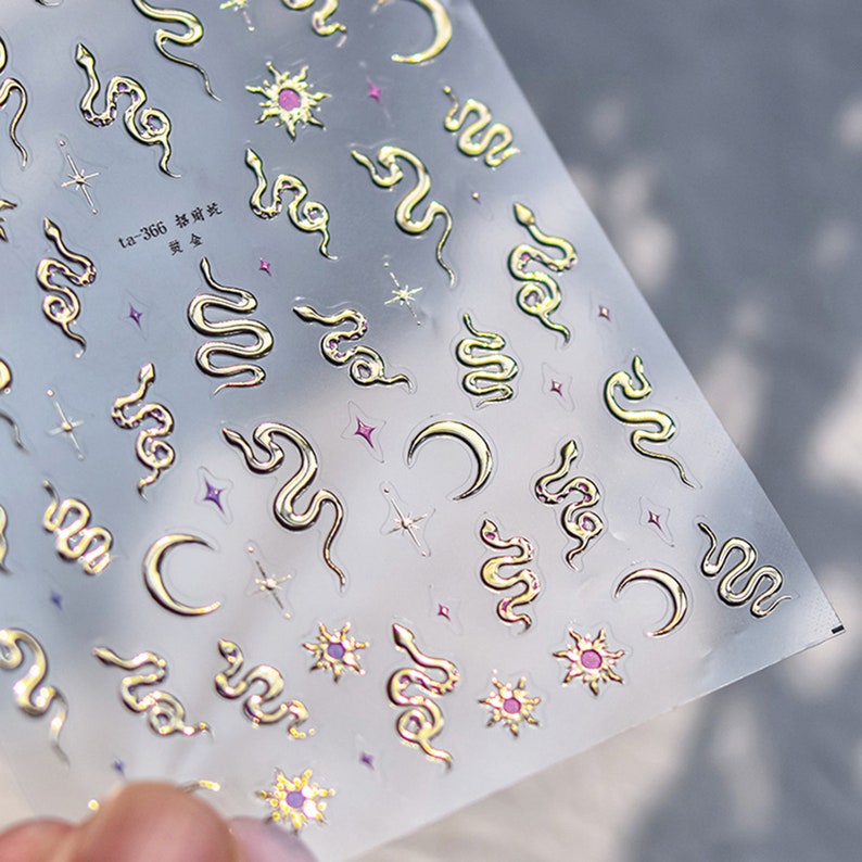 May include: Gold foil sticker sheet with a repeating pattern of snakes, moons, and stars. The sheet is labeled "ta-366  蛇  星星".
