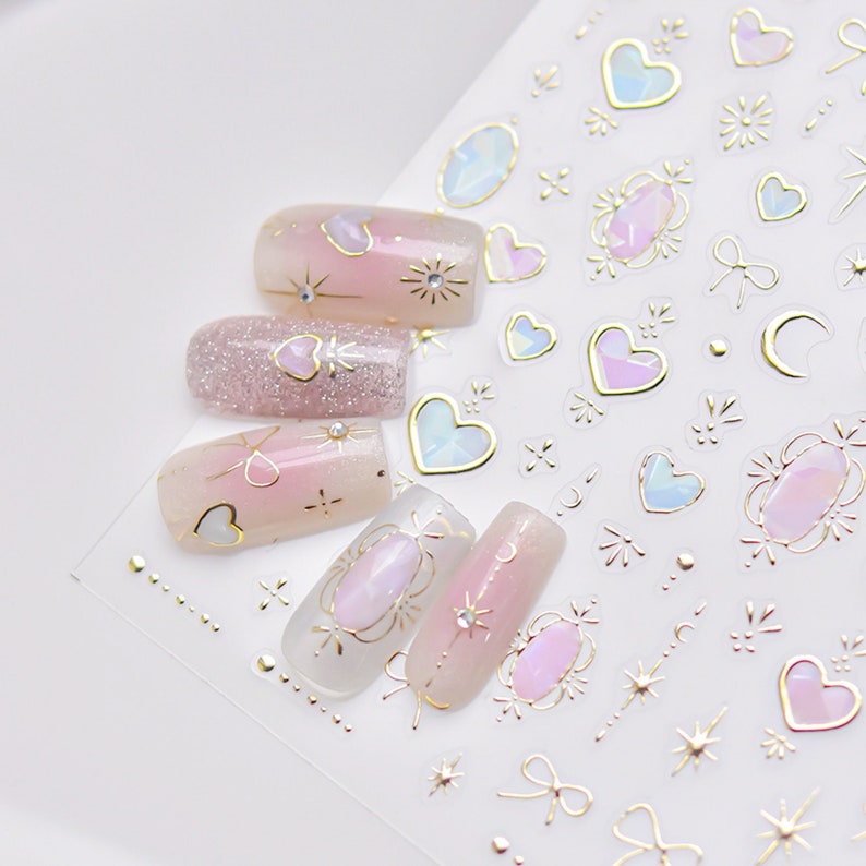May include: Nail art stickers with a pink and gold design. The stickers feature hearts, stars, moons, and other decorative elements.