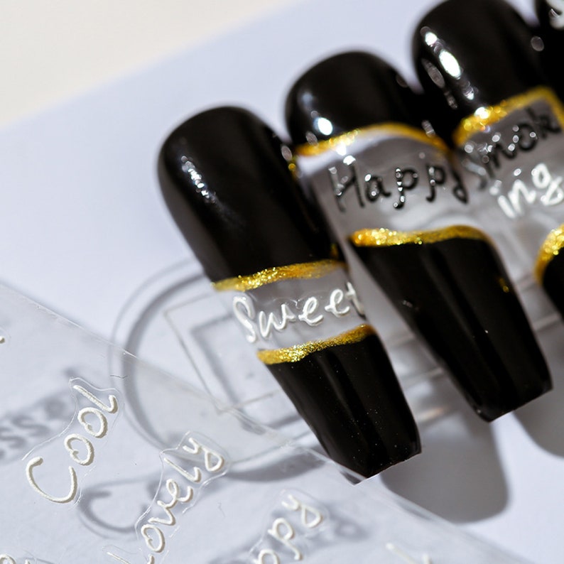 May include: Black and gold press-on nails with white lettering. The nails feature the words "Sweet", "Happy", and "Cool".