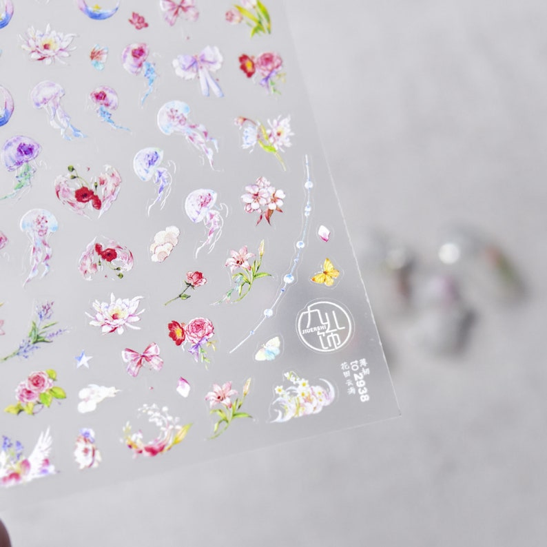 May include: A sheet of clear sticker paper with a variety of colorful stickers. The stickers feature flowers, butterflies, stars, and jellyfish. The stickers are perfect for adding a touch of whimsy to journals, planners, and other craft projects.