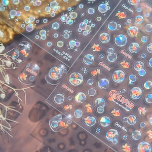May include: Clear nail art stickers featuring goldfish and bubble designs. The stickers include the text "Goldfish" and "Carpe diem". The stickers also have the text "to 5143" and "幻彩泡泡-贝壳光".