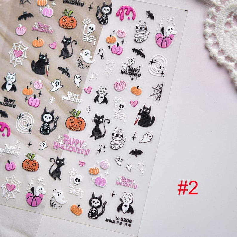 May include: Clear sheet of Halloween-themed nail art stickers. Designs include pumpkins, cats, ghosts, bats, spiderwebs, and skeletons. The text "HAPPY HALLOWEEN" is also featured. The number "#2" is visible in the corner.