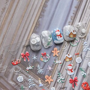 May include: A sheet of clear nail stickers with a variety of winter holiday designs, including snowmen, gingerbread men, Christmas trees, ornaments, and wreaths. The stickers also include the words "Happy" and "Merry".
