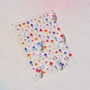 May include: A sheet of colorful nail stickers featuring mushrooms, flowers, and bunnies. The stickers are arranged in rows and are ready to be applied to nails.