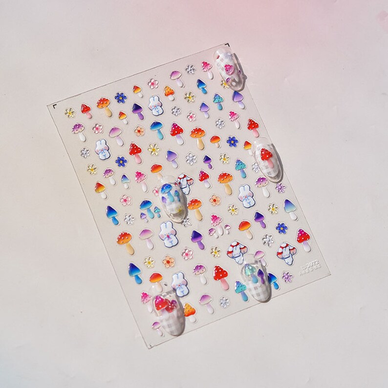May include: A sheet of colorful nail stickers featuring mushrooms, flowers, and bunnies. The stickers are arranged in rows and are ready to be applied to nails.