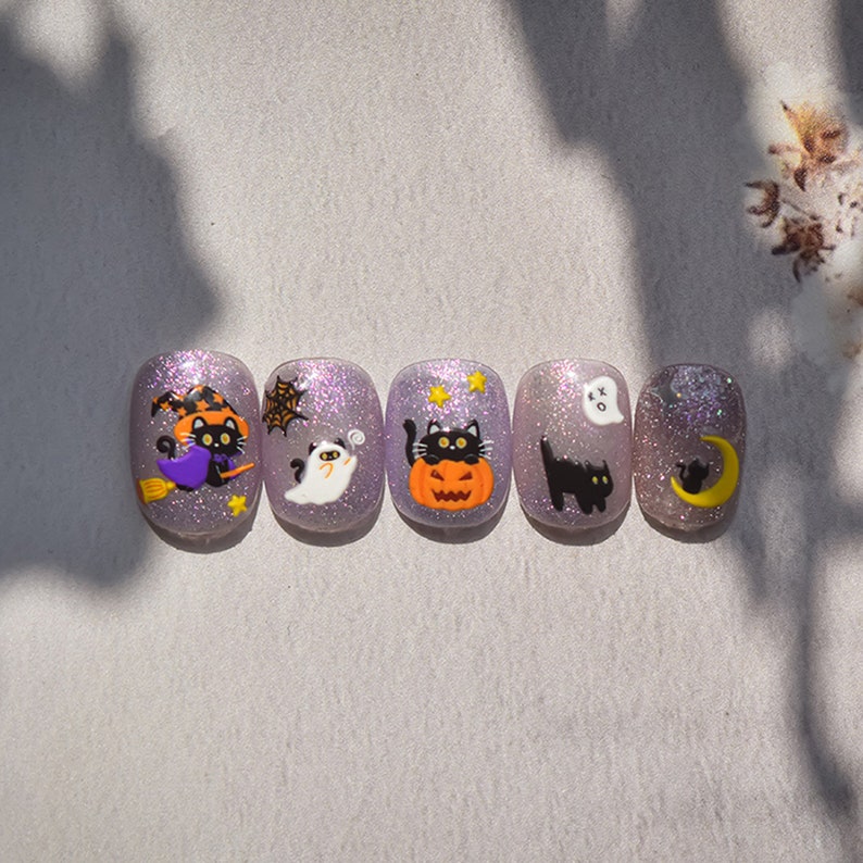 Peut inclure: Cinq designs d'ongles &agrave; paillettes violettes sur le th&egrave;me d'Halloween avec des chats noirs, un fant&ocirc;me, une citrouille, une lune croissante et une toile d'araign&eacute;e.
