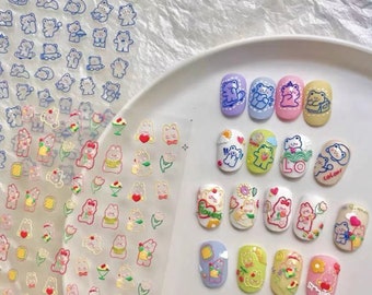 May include: A set of nail art stickers featuring cute cartoon bears with different designs. The stickers are on a clear sheet and come in a variety of colours, including pink, blue, yellow, and green. The stickers are perfect for adding a touch of whimsy to your nails.