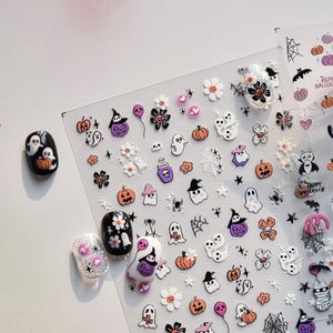 May include: Halloween-themed nail art stickers featuring pumpkins, ghosts, spiders, witch hats, and flowers in orange, purple, black, and white. Includes examples of nail art using the stickers.