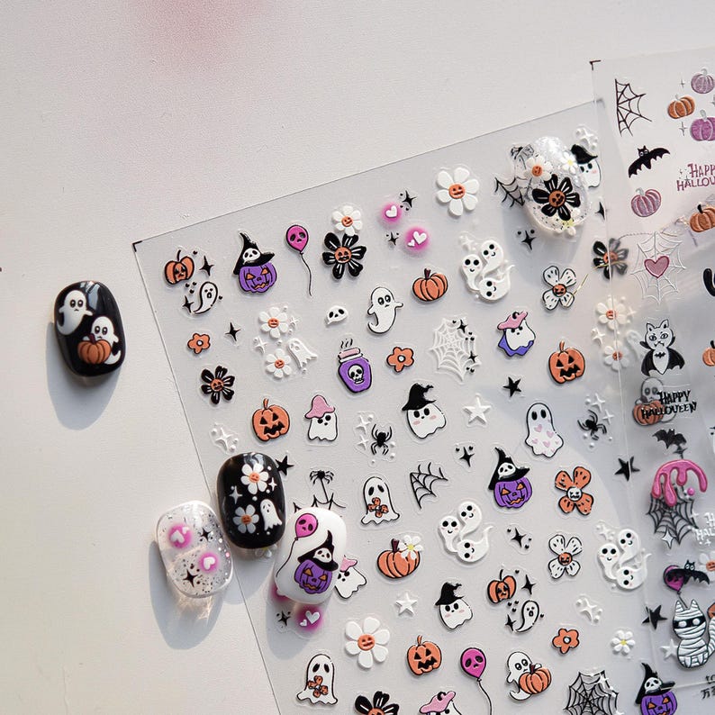 May include: Halloween-themed nail art stickers featuring pumpkins, ghosts, spiders, witch hats, and flowers in orange, purple, black, and white. Includes examples of nail art using the stickers.