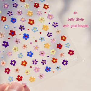 May include: A sheet of colorful jelly flower stickers with gold beads. The stickers are arranged in a repeating pattern on a clear sheet. The sheet is labeled "#1 Jelly Style with gold beads".
