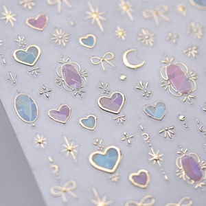 May include: A sheet of iridescent stickers with gold outlines. The stickers feature hearts, stars, moons, bows, and gemstones.