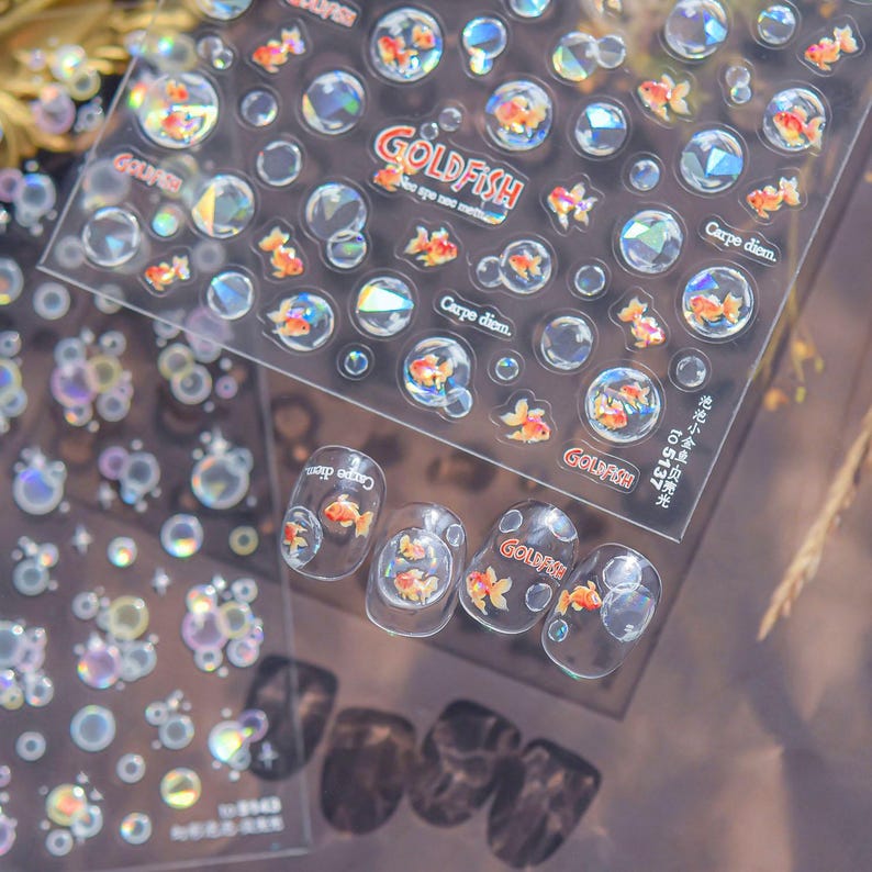 May include: Clear nail art stickers featuring goldfish and bubbles. The stickers include the text "GOLDFISH" and "Carpe diem." The design incorporates orange goldfish within clear bubbles, creating a whimsical aquatic theme.