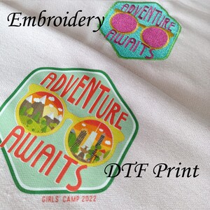 May include: Two patches with the text "Adventure Awaits" in green and white. The top patch is embroidered with pink sunglasses. The bottom patch is a printed design with yellow sunglasses and a cityscape inside the lenses. The text "Girls Camp 2022" is below the patch. The text "DTf Print" is in the bottom right corner.