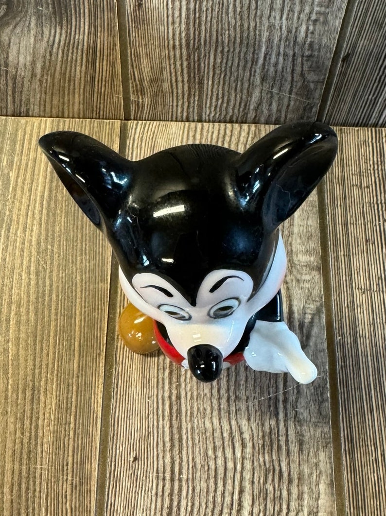 以下が含まれることがあります： ミッキーマウスの白黒のセラミック製フィギュア。ミッキーは赤いショートパンツと白い手袋を着ています。彼は右手に茶色のボールを持っています。