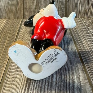 以下が含まれることがあります： 赤いシャツと黒いショートパンツを着たミッキーマウスのセラミック製フィギュア。フィギュアは足の上に立っており、右腕を上げています。フィギュアの底には「&copy; WALT DISNEY PRODUCTIONS, JAPAN」の文字があります。