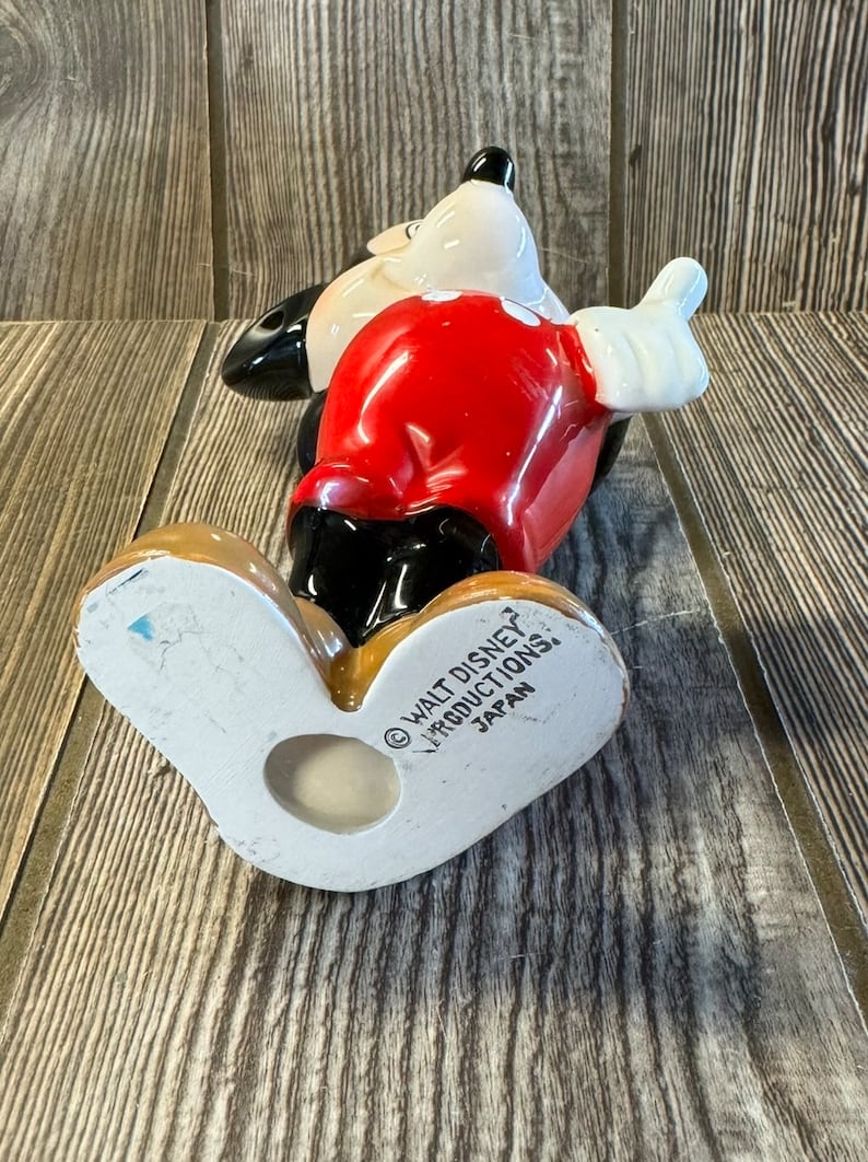 以下が含まれることがあります： 赤いシャツと黒いショートパンツを着たミッキーマウスのセラミック製フィギュア。フィギュアは足の上に立っており、右腕を上げています。フィギュアの底には「&copy; WALT DISNEY PRODUCTIONS, JAPAN」の文字があります。