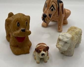 May include: Four ceramic dog figurines. The figurines are in various poses and have different facial expressions. The dogs are brown, white, and black.