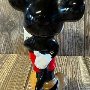 以下が含まれることがあります： ミッキーマウスの黒いセラミック製フィギュア。赤いショートパンツと白い手袋を着用しています。尻尾は後ろに巻かれています。