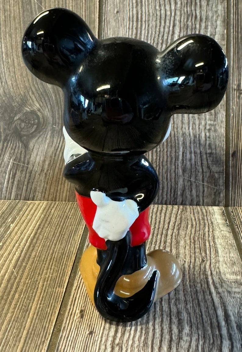 以下が含まれることがあります： ミッキーマウスの黒いセラミック製フィギュア。赤いショートパンツと白い手袋を着用しています。尻尾は後ろに巻かれています。