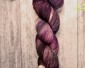 Può includere: Un gomitolo di filato viola e crema con un motivo di colore variegato. Il filato è attorcigliato in una bobina sciolta.