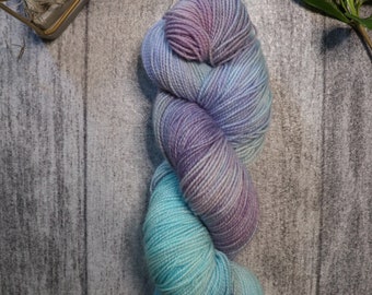 May include: A skein of yarn in shades of purple, blue, and teal. The yarn is wound into a ball and is ready to be used for knitting or crocheting.