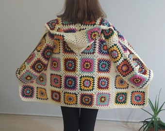 May include: A crocheted cardigan with a hood, featuring a colorful patchwork design of squares in various shades of pink, yellow, blue, green, and orange. The cardigan is made with a cream-colored yarn.