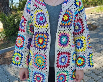 May include: A crocheted cardigan with a hood, featuring a colorful geometric pattern of squares with circular designs. The cardigan is made with a beige yarn and has a loose fit.