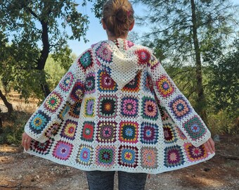 May include: A white crocheted cardigan with a hood, featuring a colorful patchwork design of squares. The cardigan is made with a variety of colors, including red, blue, green, yellow, and purple.
