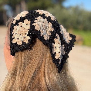 May include: A black and tan crochet headscarf with a floral pattern. The head covering is made of yarn and is worn on the head. The headscarf is a square shape and is worn on the head.