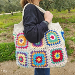 May include: A large crocheted tote bag with a colorful granny square pattern. The bag is made of beige yarn and features squares with shades of pink, blue, green, yellow, and red.