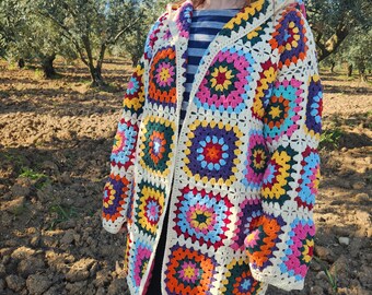 May include: A colorful, hooded crochet jacket featuring a patchwork design. The jacket showcases vibrant squares in shades of pink, orange, yellow, green, and purple, bordered by a cream-colored yarn. The open front design and long sleeves create a cozy, bohemian aesthetic.