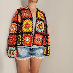 May include: A black crochet cardigan with colorful granny square patches. The cardigan has a long sleeve and a relaxed fit.