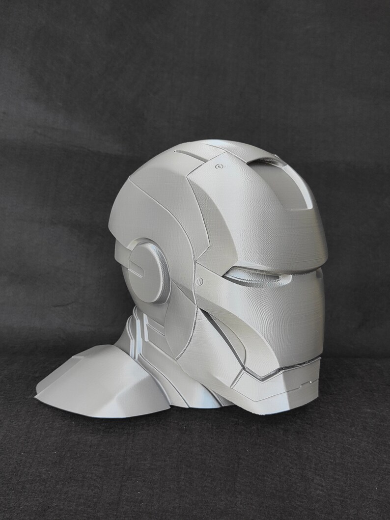 May include: A gray 3D printed model of a helmet with a faceplate and a neck piece. The helmet is designed to look like a futuristic or sci-fi helmet.