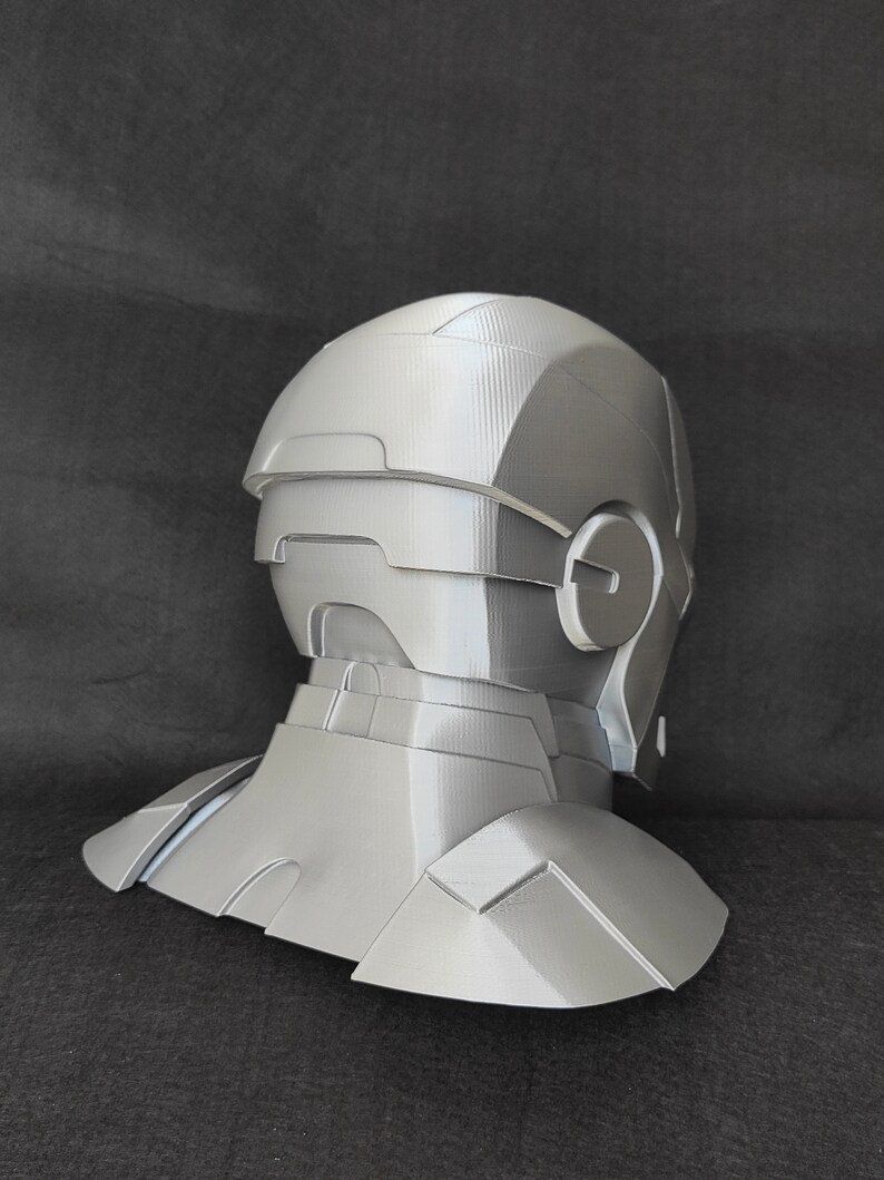 May include: A gray 3D printed helmet with a neck piece. The helmet has a textured surface and a design that resembles a futuristic robot.