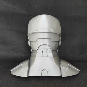 May include: A gray 3D printed helmet with a neck piece. The helmet has a visor and a textured surface.