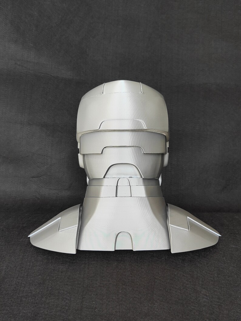 May include: A gray 3D printed helmet with a neck piece. The helmet has a visor and a textured surface.