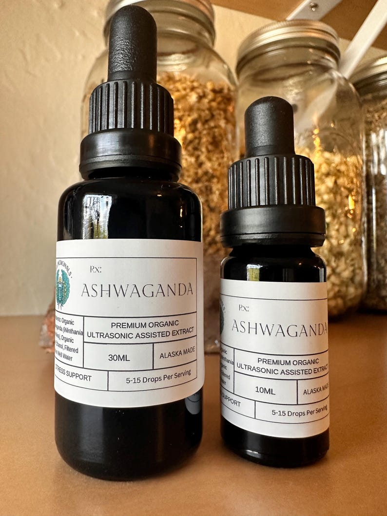 Puede incluir: Dos frascos cuentagotas de vidrio negro de extracto de Ashwaganda. Las etiquetas dicen "Premium Organic Ultrasonic Assisted Extract" y "Alaska Made". Una botella es de 30 ml, la otra de 10 ml. Las botellas est&aacute;n sobre una superficie de madera.