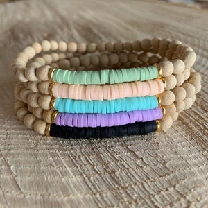 May include: A set of five bracelets stacked on top of each other. The bracelets are made of natural wood beads and colorful silicone beads. The silicone beads are in shades of green, pink, blue, purple, and black.