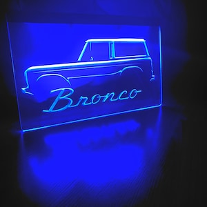 May include: Blue neon sign with the silhouette of a Ford Bronco and the word "Bronco" underneath.