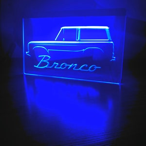 May include: A blue neon sign with the silhouette of a Ford Bronco and the word "Bronco" underneath.